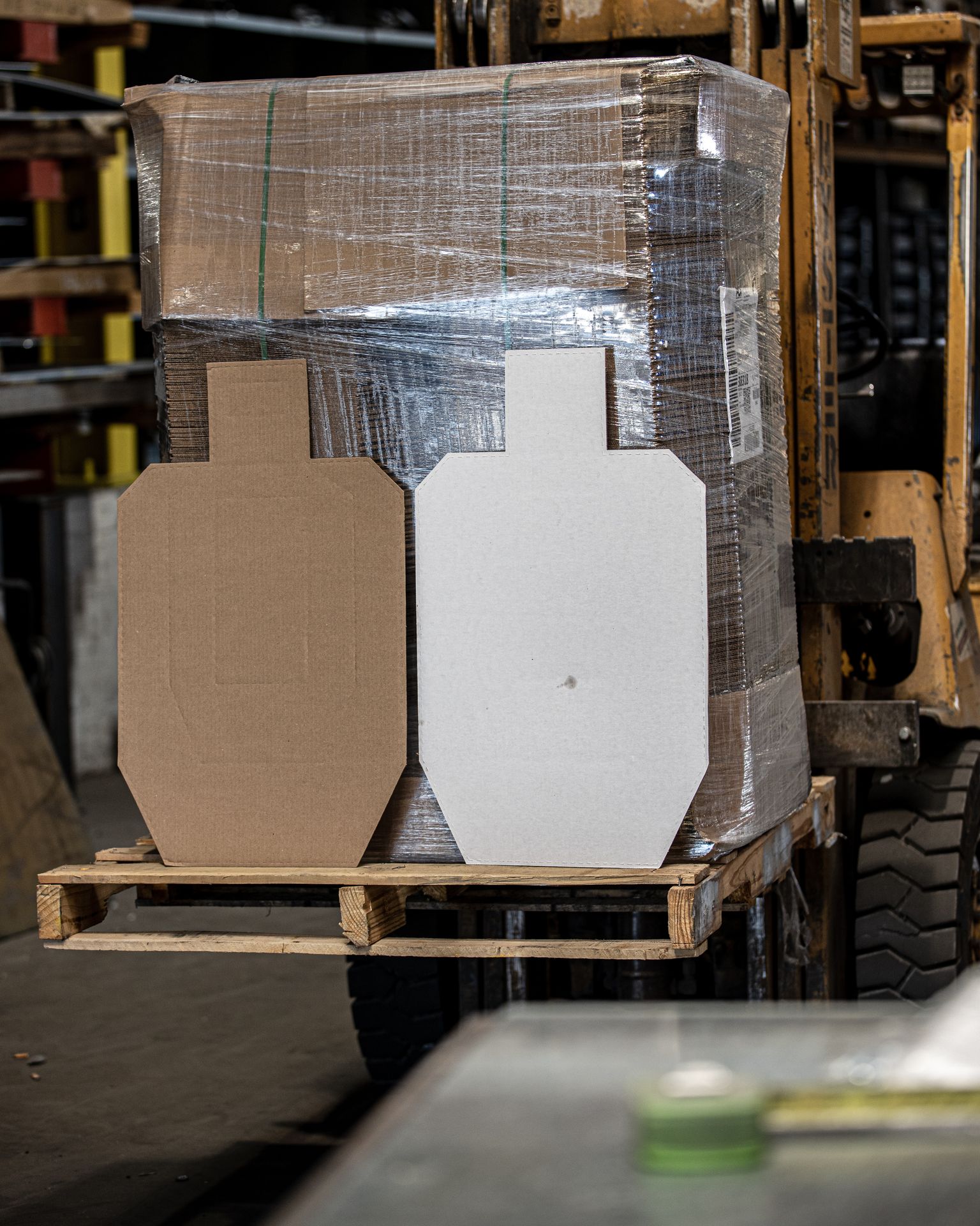 Tan and white official USPSA cardboard targets standing in front of a shrink-wrapped skid on a pallet