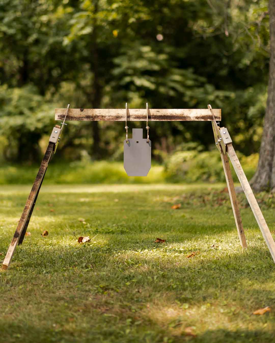 AR500 steel gong hanging from a wooden A-frame gong stand on a grass shooting range